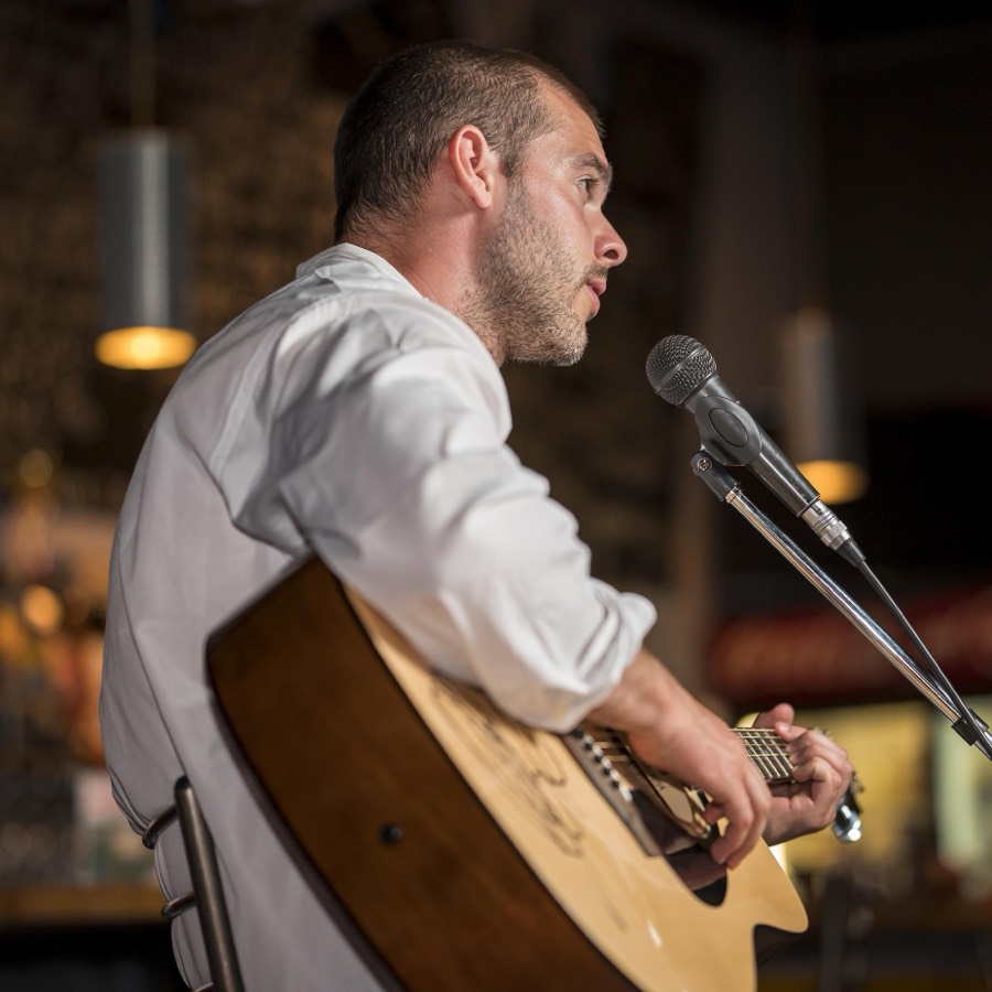 A guitarist singing into a mic in a small warmly lit venue